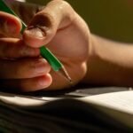Detailed view of a hand writing with a pencil in a notebook, implying study or creativity.