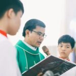 A priest recites a holy book during a religious ceremony with altar boys in a church.