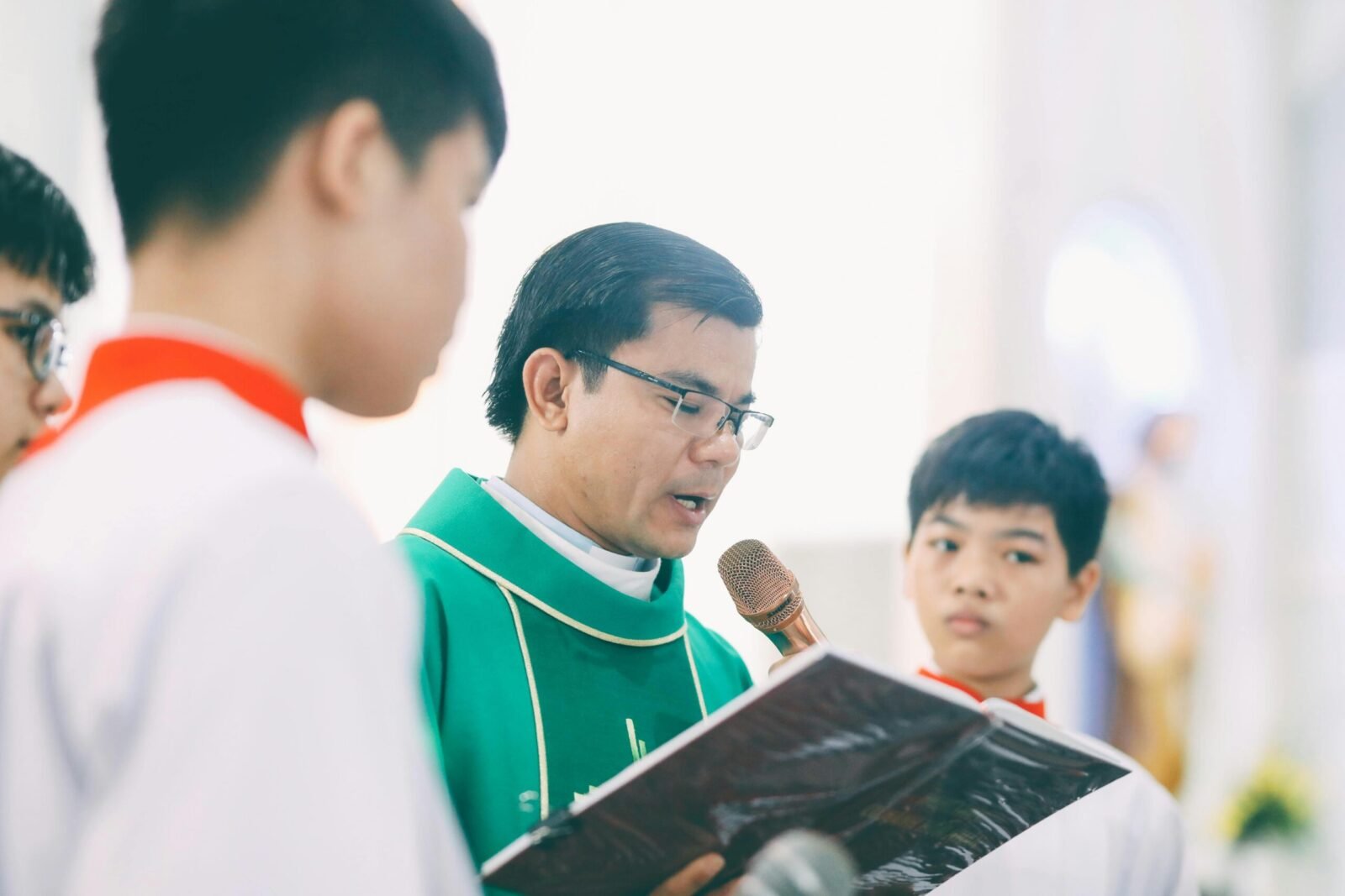 A priest recites a holy book during a religious ceremony with altar boys in a church.
