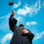 A man in a graduation gown throwing a hat in the air